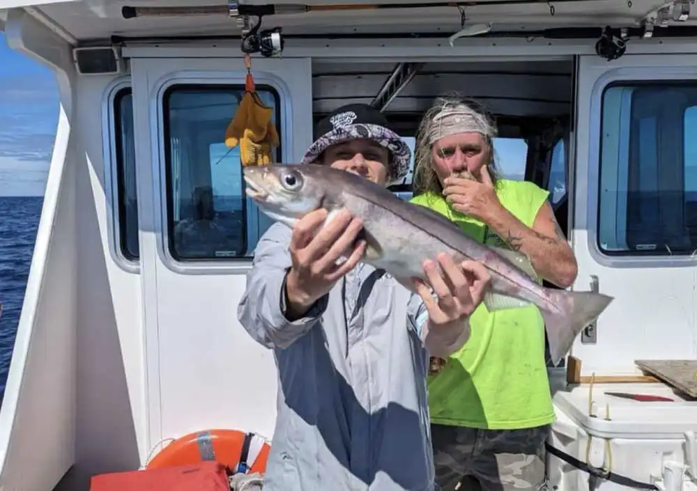 Tuna Tail Charters guests celebrate their fishing success as a man and woman stand together in the water near Gloucester.